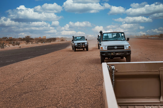 Off-road vehicles drive on a dusty, open road.